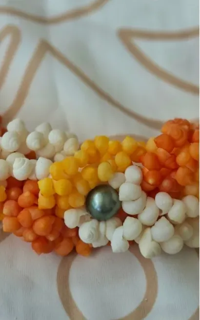 Bracelet de petits coquillages orange, jaunes et blancs montés en fleurs autour d’une perle grise.